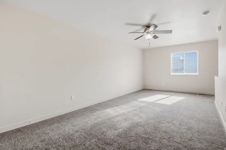 Plush carpet flooring, neutral wall tones, window with horizontal blinds, and a ceiling fan with integrated lighting