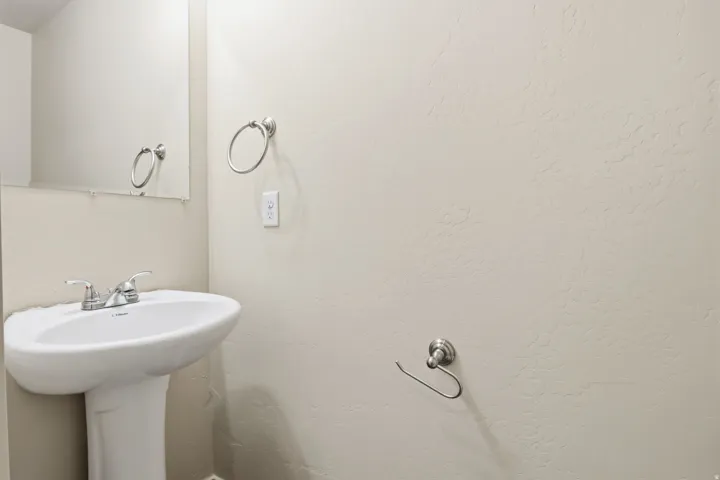 Pedestal sink with chrome faucet, wall-mounted mirror, and brushed nickel hardware