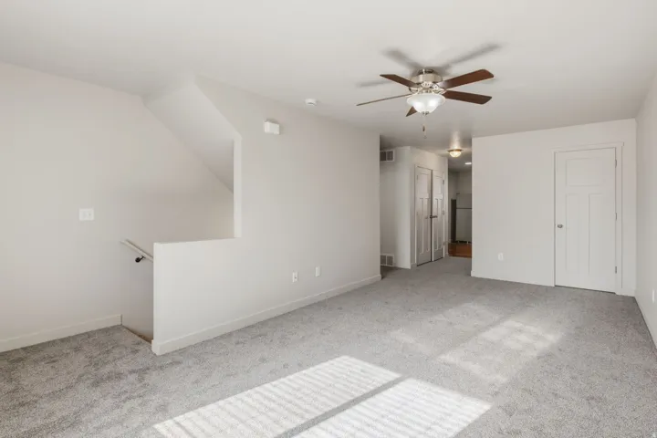 Carpeted living space with a ceiling fan light fixture, white interior doors, and a staircase