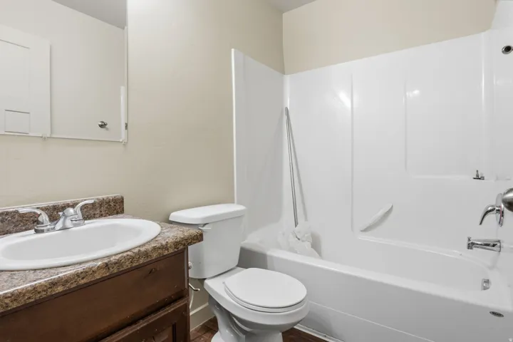 Bathroom featuring a white bathtub with shower, toilet, wood-finish vanity with a built-in sink, and a mirrored medicine cabinet