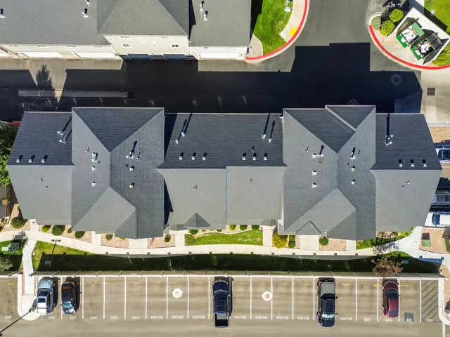 Multi-unit property with dark shingle roofing, designated parking spaces, and concrete pathways