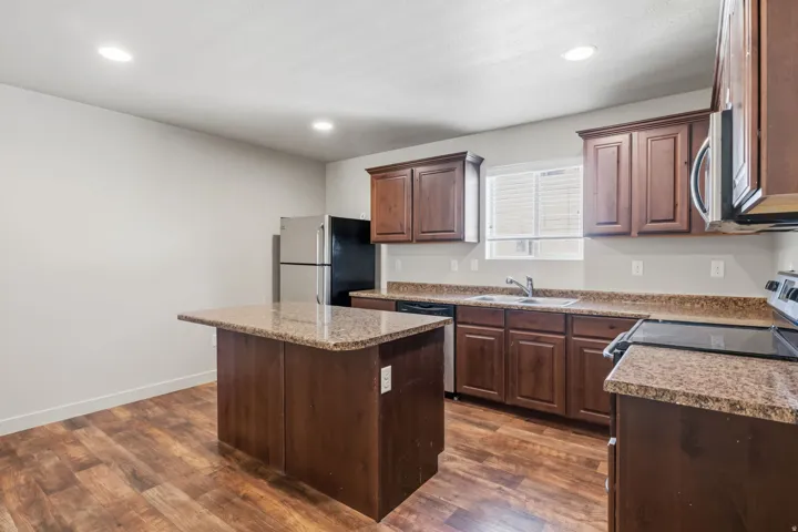 Kitchen featuring wood-finish flooring, dark wood cabinetry, granite-style countertops, an island with extended counter space, and stainless steel appliances