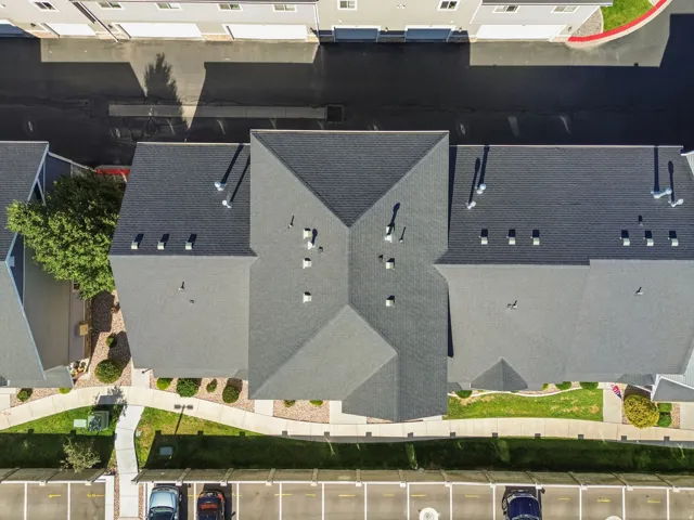 Pitched shingle roofing with multiple ventilation fixtures, surrounding landscaped grounds, and dedicated parking spaces