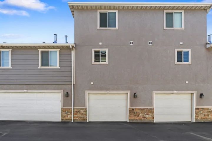 Multi-level exterior with stucco and horizontal siding, multiple windows, and integrated garages with stone veneer accents
