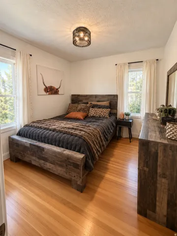 Hardwood flooring, two windows with natural light, a ceiling-mounted light fixture, and a built-in wood-finish bed frame