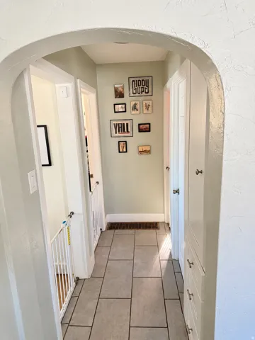 Arched entryway leading to a hallway with rectangular tile flooring and built-in cabinetry
