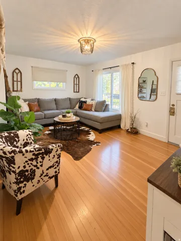 Hardwood flooring throughout, recessed window with roller shade, large window with curtain rod and drapes, and an overhead decorative light fixture