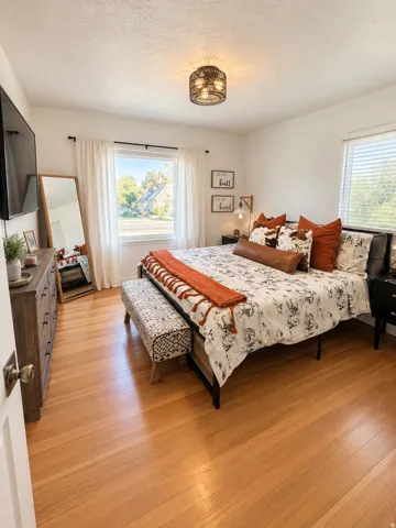 Hardwood flooring, white walls, flush mount ceiling light fixture, double windows with blinds, and transom windows