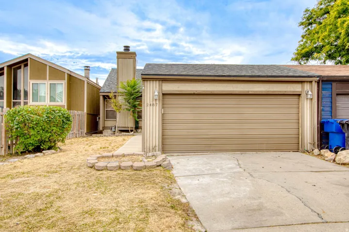 Attached garage with a concrete driveway, exterior wall lighting, and a front walkway