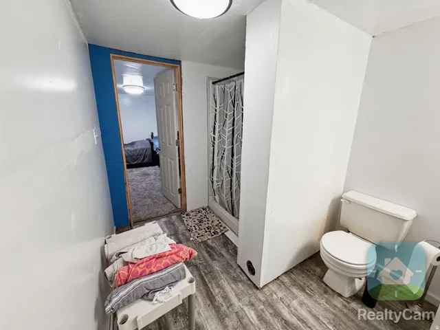 Wood-finish flooring with a stand-up shower enclosure, white toilet, and recessed lighting