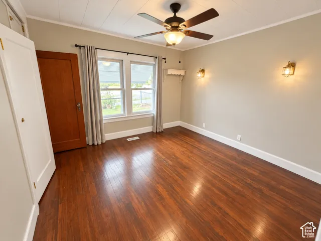 Room featuring wood-finish flooring, dual wall-mounted sconce lighting, a multi-blade ceiling fan with integrated light fixture, and a solid wood door