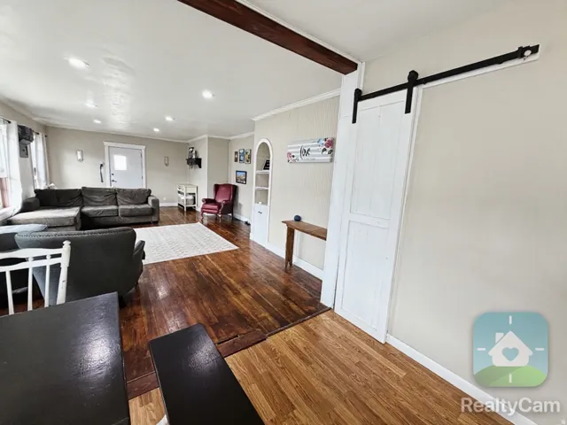 Wood-finish flooring, exposed ceiling beam, recessed lighting, white barn door, and built-in shelving