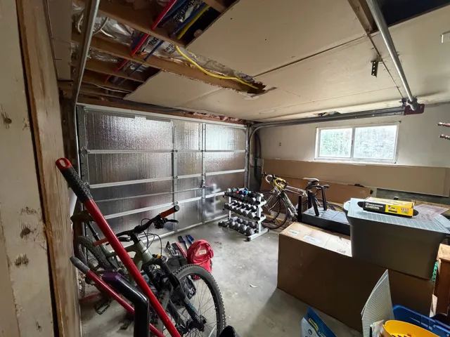 Insulated garage door, exposed ceiling joists, concrete flooring, and horizontal window