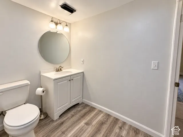 Bathroom featuring a white vanity cabinet with an integrated countertop and basin, circular wall mirror, three-light vanity fixture, and wood-finish flooring