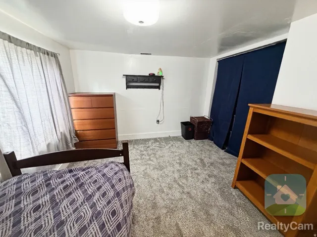 Carpeted room with a ceiling-mounted light fixture, white walls, and a window with curtains