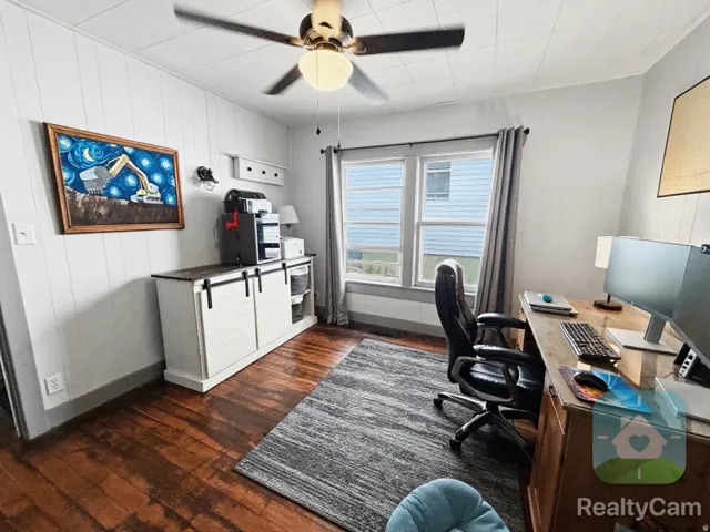 Wood-finish flooring, white paneled walls, ceiling fan with integrated lighting, and a multi-pane window