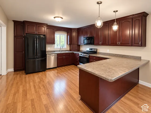 Kitchen featuring dark wood cabinetry, an extended peninsula, wood-finish flooring, and a suite of integrated appliances