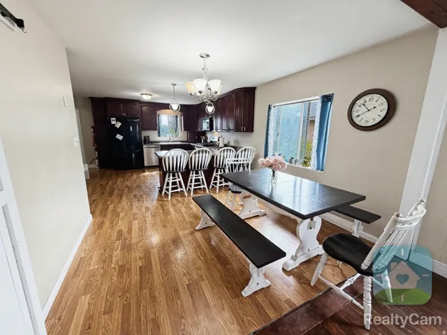 Open-concept kitchen and dining area featuring wood-finish flooring, dark wood cabinetry, a breakfast bar with seating, and a multi-light chandelier
