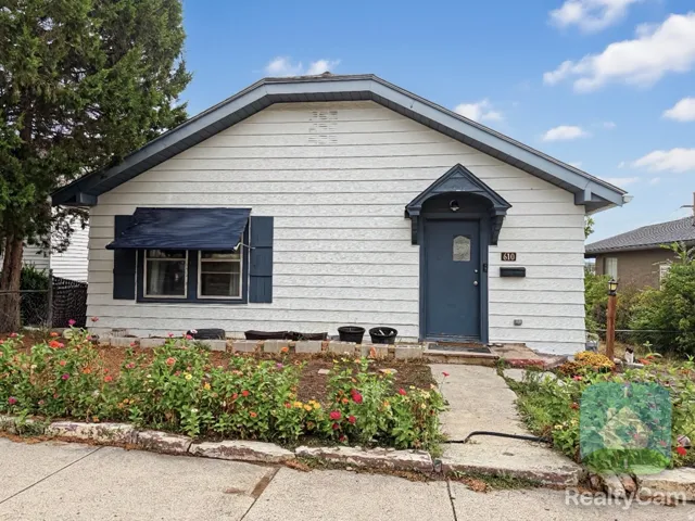 Exterior featuring white siding, a covered entry, dark-paneled door, and a landscaped front garden with a stone border