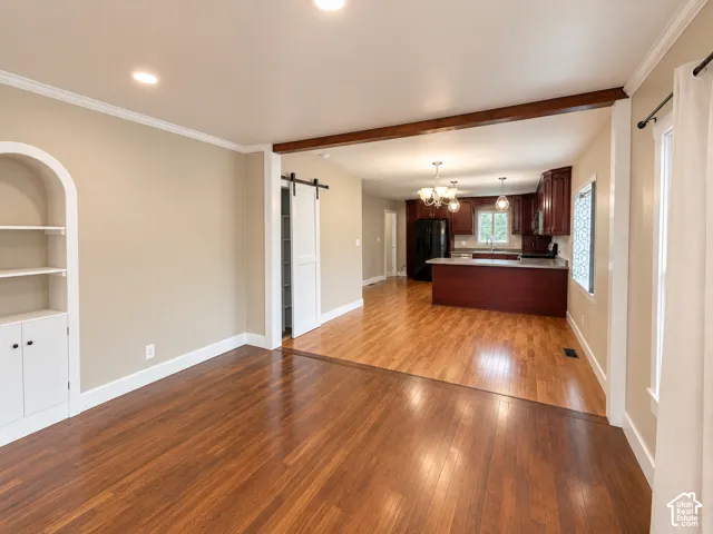 Wood-finish flooring, built-in arched display shelving with lower cabinetry, sliding white barn door, and a kitchen featuring dark wood cabinetry and a peninsula