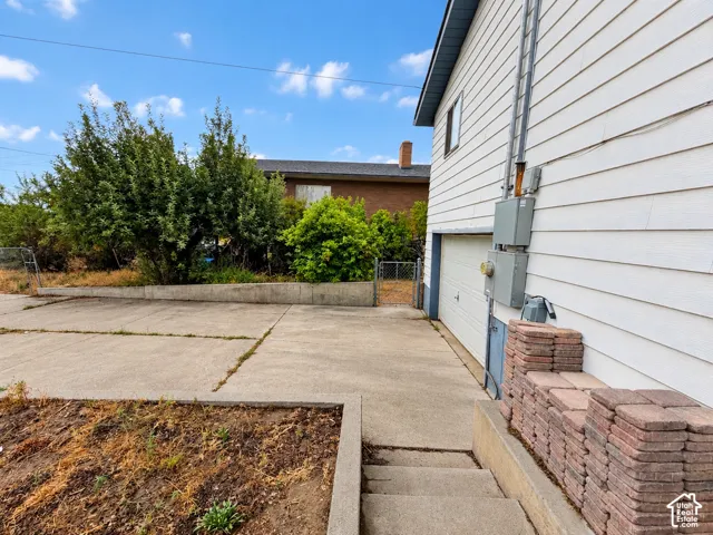 Concrete driveway, attached garage, and retaining walls featuring concrete construction with metal perimeter fencing