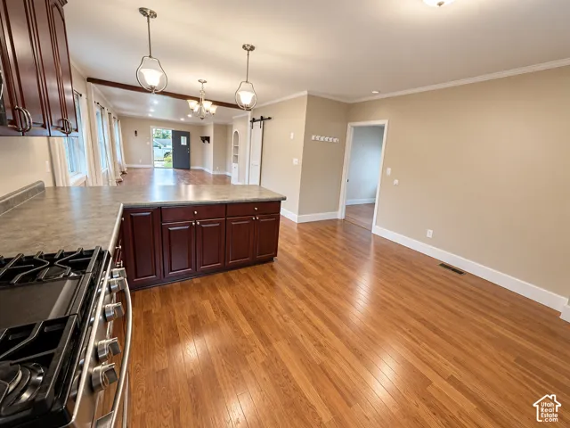 Kitchen featuring dark wood cabinetry, a peninsula with stone-finish countertop, stainless steel gas range, wood-finish flooring, and pendant lighting