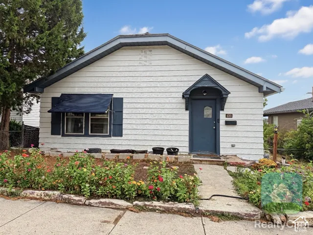 Exterior featuring white siding, a covered entry, dark-paneled door, and a landscaped front garden with a stone border