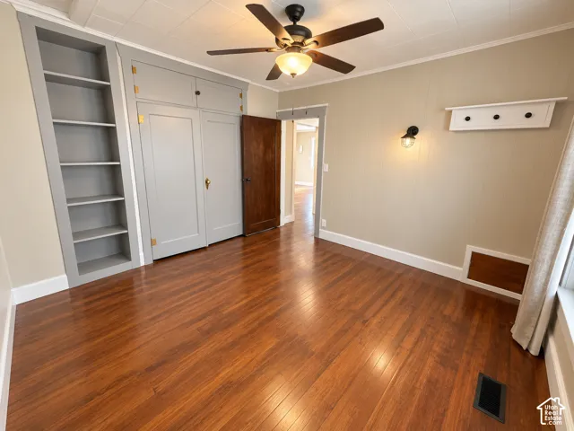 Interior space featuring wood-finish flooring, built-in shelving, custom cabinetry, a ceiling fan with integrated lighting, and wall-mounted sconce lighting