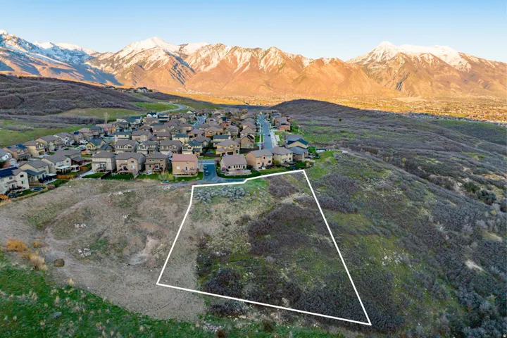 Expansive lot with a sloping terrain, surrounded by natural shrubbery and distant snow-capped mountains