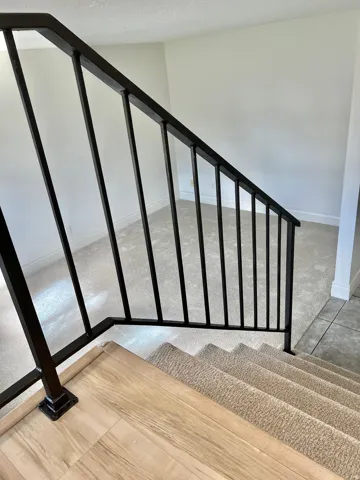 Black metal stair railing with wood-finish flooring at the landing, carpeted stairs, and light neutral wall colors