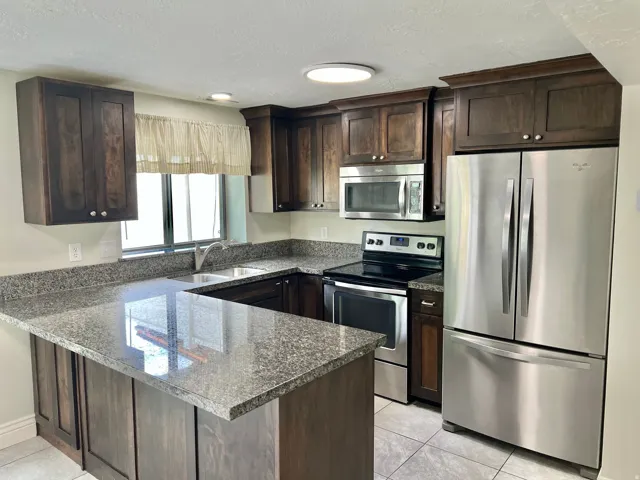 U-shaped kitchen featuring dark wood cabinetry, stainless steel appliances, speckled countertops, and a double basin sink