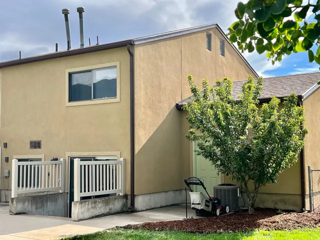 Stucco exterior featuring a pitched roof, a sliding window, and a ground-level patio with a privacy fence