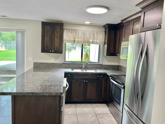 Kitchen featuring dark wood-finish cabinetry, speckled countertops, stainless steel appliances, and tile flooring