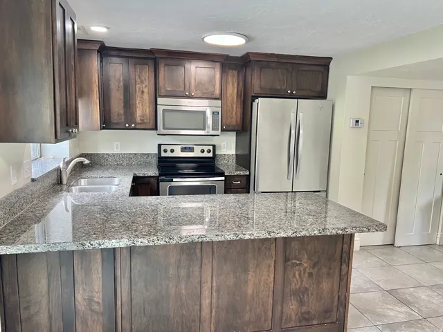 Kitchen featuring dark wood cabinetry, granite countertops, stainless steel appliances, a double basin sink, and tile flooring