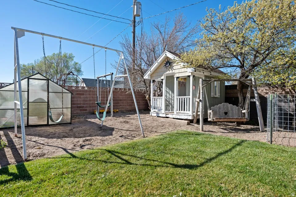 Expansive backyard featuring a manicured lawn, a detached greenhouse, a wooden playhouse, and a swing set