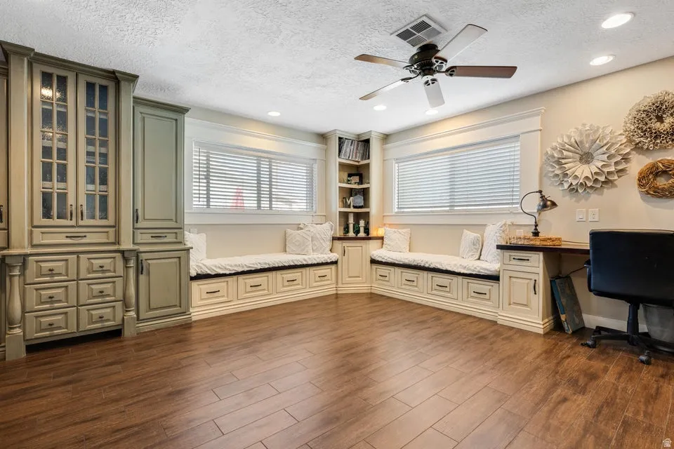 Wood-finish flooring, built-in cabinetry with glass panel doors, recessed lighting, ceiling fan, and built-in window seating with storage