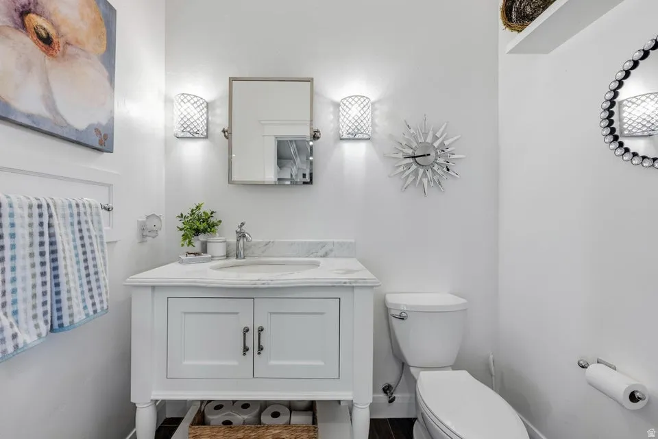 White vanity with a single basin and chrome faucet, under-sink storage, wall-mounted mirror, and decorative sconce lighting