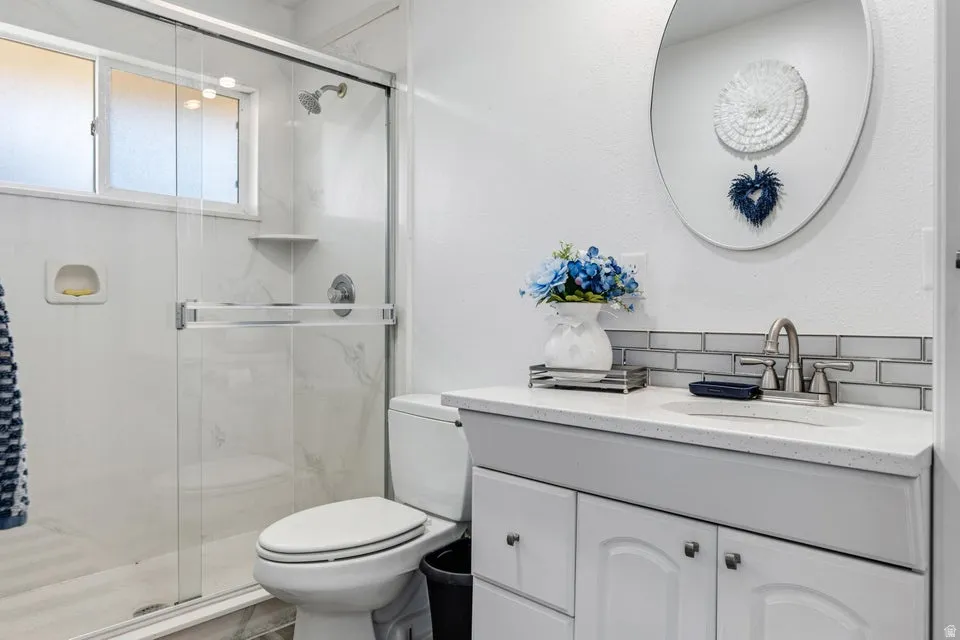 Glass-enclosed shower with a window, white vanity with an integrated sink, polished chrome faucet, and subway tile backsplash
