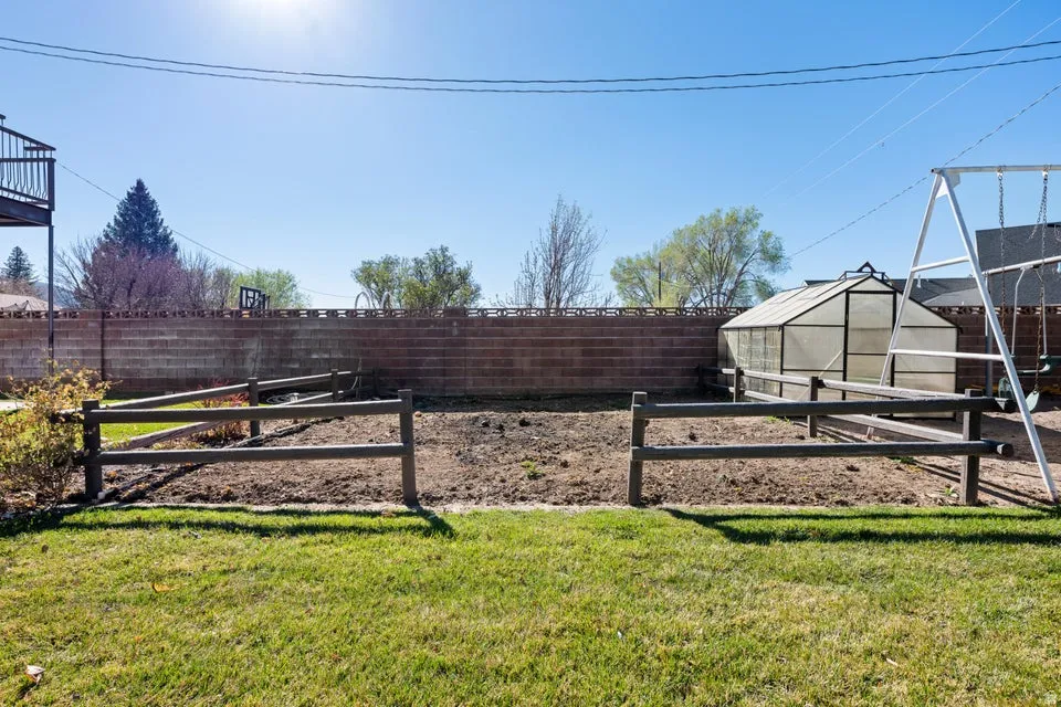 Expansive backyard featuring a manicured lawn, a raised garden bed with a wooden fence, a clear-paneled greenhouse, and a brick privacy wall