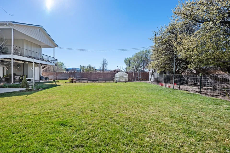 Expansive lawn with a two-story exterior deck, integrated covered patio, fenced perimeter, and a greenhouse structure