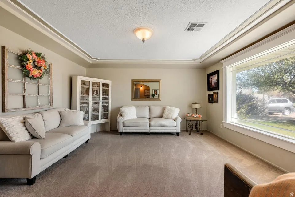Recessed ceiling with layered crown molding, large picture window, built-in display cabinet with glass doors, and wall-to-wall carpeting