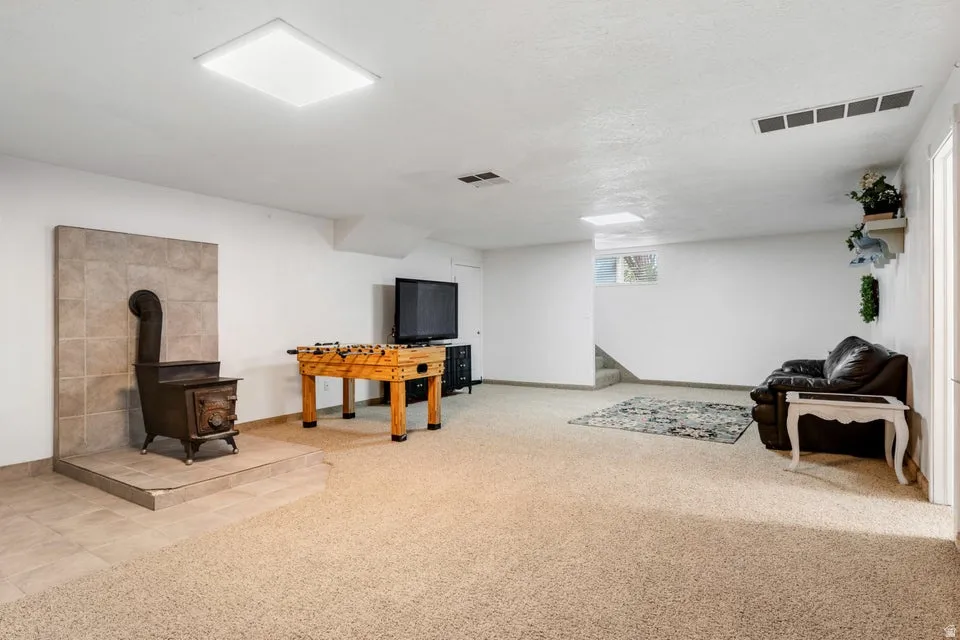 Spacious room featuring a wood-burning stove with a tiled surround, recessed lighting, and soft carpeting