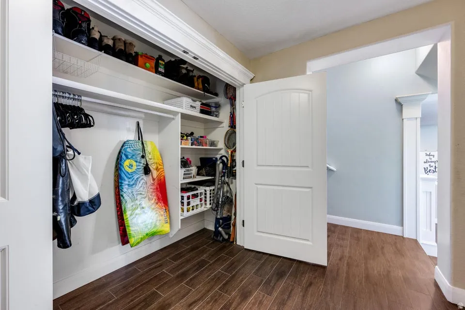 Wood-finish flooring with a closet featuring white panel doors, built-in shelving, and hanging rods