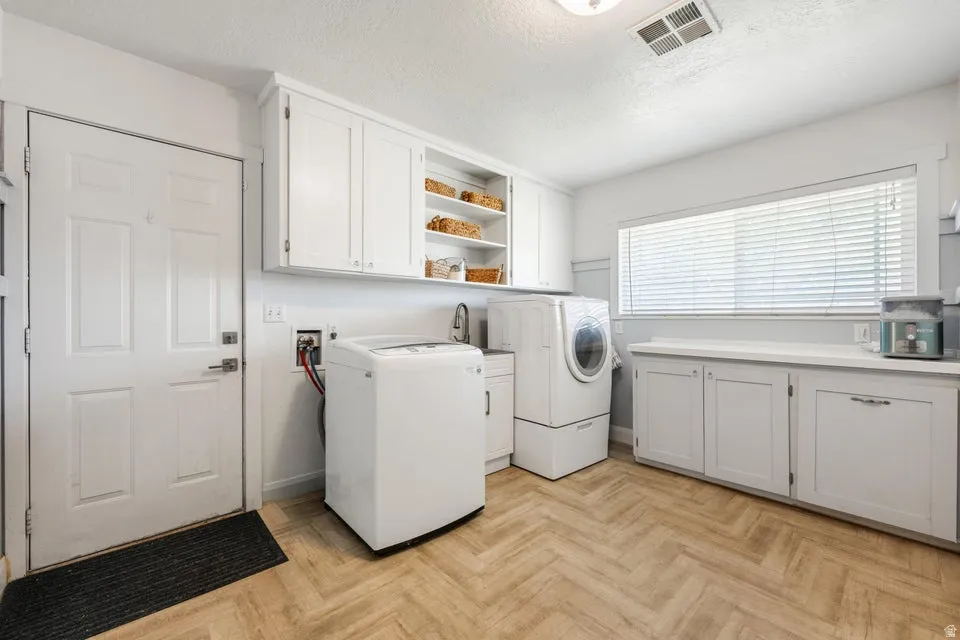 Laundry room featuring herringbone-pattern wood-finish flooring, white cabinetry, a built-in sink, and a large window