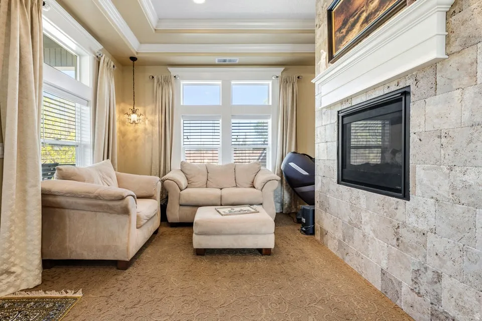 Tray ceiling with crown molding, recessed lighting, and a stone-clad fireplace with a white mantel and a dark metal firebox