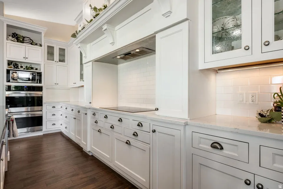 White shaker cabinetry, built-in double ovens, built-in microwave, white subway tile backsplash, and light-toned countertops