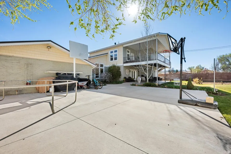 Expansive concrete patio with a basketball hoop, offering direct access to a two-story residence with a covered balcony and lower-level patio
