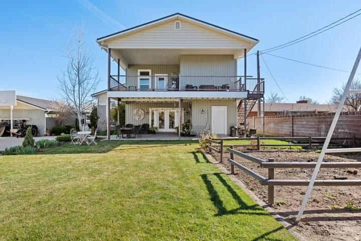 Two-story residence with a covered patio, upper-level balcony, exterior staircase, and an expansive lawn