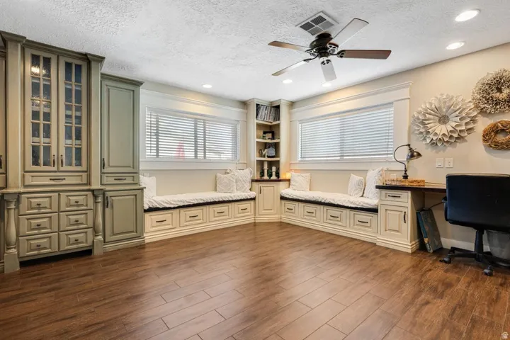 Wood-finish flooring, built-in cabinetry with glass panel doors, recessed lighting, ceiling fan, and built-in window seating with storage