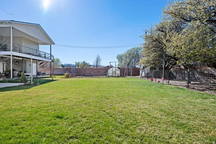 Expansive lawn with a two-story exterior deck, integrated covered patio, fenced perimeter, and a greenhouse structure